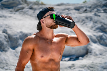 Portrait of a handsome halfnacked bodybuilder man on a mountain with a bottle of water.