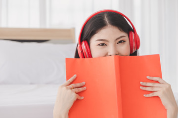 Beautiful woman wearing red headphones listening music and read orange book  happy.