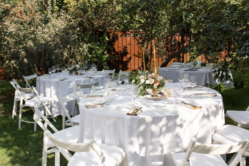 Wedding table setting decorated with fresh flowers in a brass vase. Wedding floristry. Banquet table for guests outdoors with a view of green nature. Bouquet with roses, eustoma and eucalyptus leaves