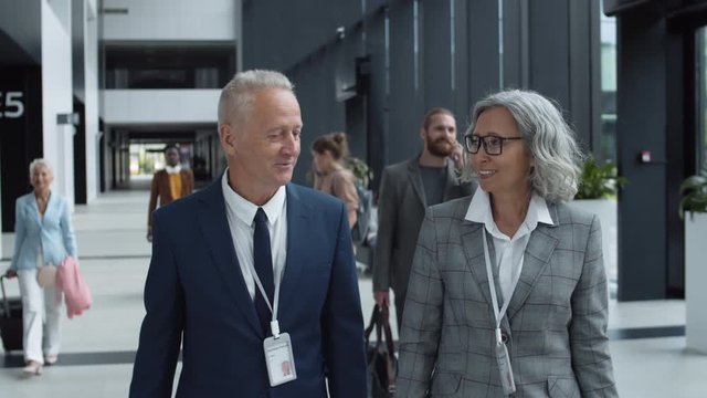 Medium shot of senior Caucasian businessman and businesswoman going together along airport and having talk