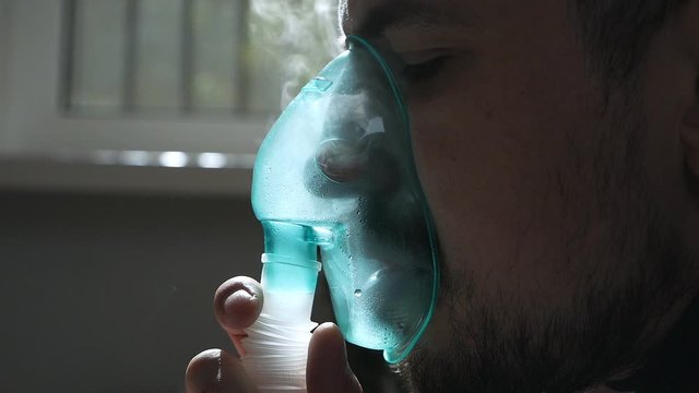 A sick person inhales through a nasal inhaler while sitting on a sofa. Close up face. Use a nebulizer and inhaler for treatment