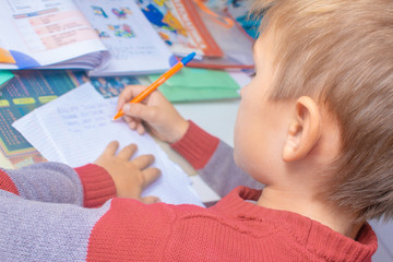A boy writes English words by hand on traditional white paper in a notebook. The boy writes his...