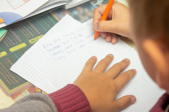 A boy writes English words by hand on traditional white paper in a notebook. The boy writes his first test on English. Child writing, spelling and education. Boy learns english. English writing skills