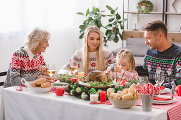 smiling family members sitting at table and celebrating Christmas