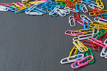 Lot of scattered different colors paper clips red, green, blue, yellow, white and pink for office work or education lies in corner on dark scratched concrete table. Space for text - Powered by Adobe