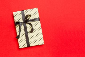 Gift box with black bow for Christmas or New Year day on red background, top view with copy space