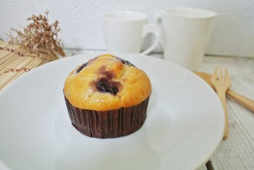 Blueberry muffin in a white plate on a vintage white wooden table.