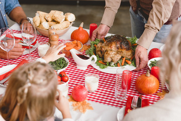 cropped view of grandfather putting on table plate with turkey in Thanksgiving day