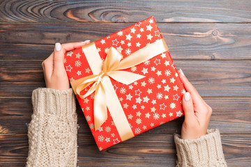 Top view of female hands holding christmas or other holiday handmade present box package in the palms, flat lay table background with copy space