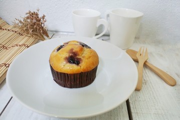 Blueberry muffin in a white plate on a vintage white wooden table.