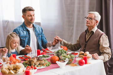 father, granddaughter and grandfather holding hands and prying in Thanksgiving day