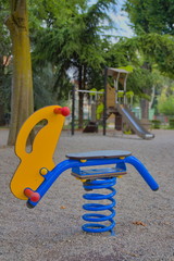 Children's swing with a bright blue spring, a children's slide is visible in the distance. Summer, empty playground. Europe, Italy