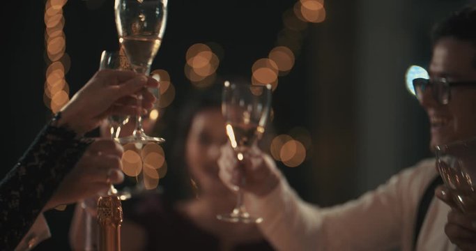 Multiracial young mans and womans wearing fashion wear clinking glasses with champagne, happy asian american and caucasian friends celebrating xmas, new year or birthday party indoors