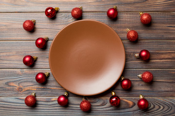 Top view of festive plate with red baubles on wooden background. Christmas decorations and toys. New Year advent concept