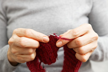 Closeup womans hands knits red burgundy wool yarn with knitting needles. Shallow focus.