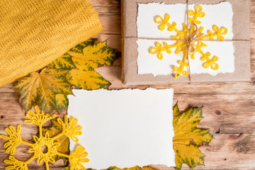 Gift box.kraft packaging.Mockup torn paper for your notes. Autumn bright dry leaves.Yellow knitted sweater.wooden background.flat lay.Autumn cozy fall concept. Flat lay,top view, copy space