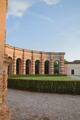 Ancient wall with arches and part of a well-kept garden. Blue sky, the rays of the evening sun, a place for writing text