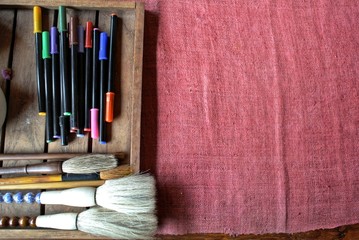 Crimson woven fabric background and crayon brush set on wooden tray
