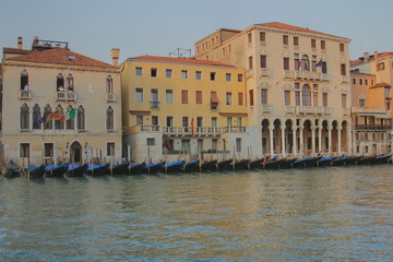 Gondolas stand in a row near an old building in Venice, view through the canal, evening light