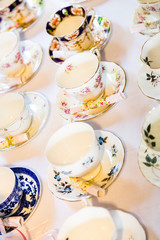Decorative china teacups and matching saucers on white table cloth.