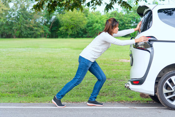 Side View of Woman pushing her car along the load after breakdown.