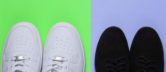 White fashionable sneakers and black suede shoes on colored background. Top view.