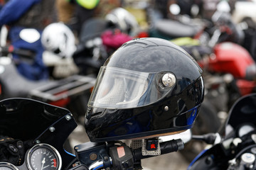 Closeup bkack moto helmet on motorcycle handlebars and motorbikes on blurred background