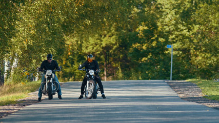 Two bikers on their bikes are standing on the road