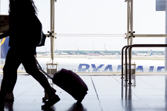 Barcelona, Spain - August 11, 2019: Passengers walking with luggage in the airport terminal, with Ryanair airplane in the background