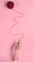 Female hand holding skein of thread through torn pink paper. Minimalistic creative medicine concept