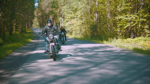 Two bikers are riding a dusty road in the forest