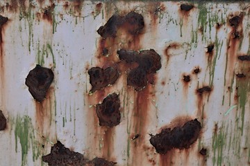 An iron surface painted white with green smudges, with large spots of rust.