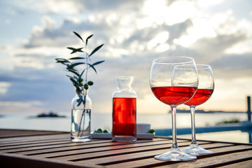 two glasses of rose wine with  olives against blue water on a pier..