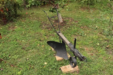 An old wooden plow with metal parts stands in the garden.