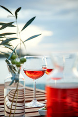 two glasses of rose wine with  olives against blue water on a pier..