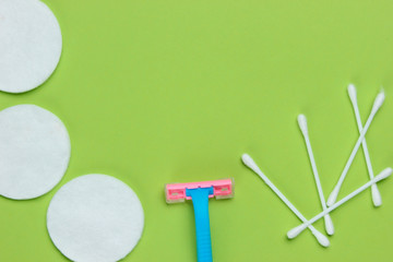 Beauty still life, minimalism. Plastic epilator razor with cotton circles and ear sticks on green background. Women's accessories for beauty care. Top view. Copy space