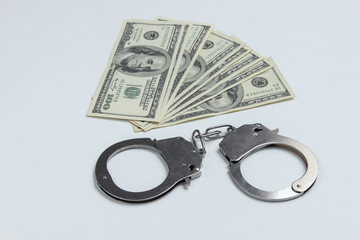 Steel handcuffs and one hundred dollar bills on a white background. Crime, corruption concept