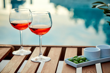 two glasses of rose wine with  olives against blue water on a pier..