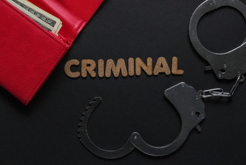 Steel handcuffs and red leather wallet on black background. Criminal, corruption concept