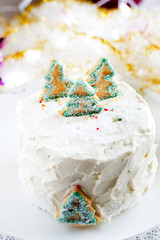 New Year's Christmas festive homemade cake with white butter cream glaze frost decorated with green Christmas tree cookies with garlands and lights on background. Bakery style cake for the celebration