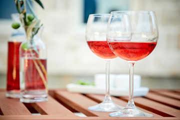 two glasses of rose wine with  olives against blue water on a pier..