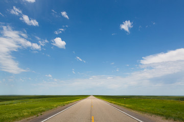 Empty two lane highway beneath calm blue sky.