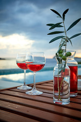two glasses of rose wine with  olives against blue water on a pier..