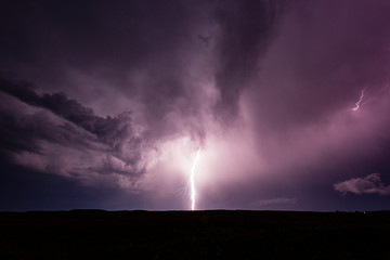 Naklejka na ściany i meble Powerful bolt of lightning striking the ground during thunderstorm.