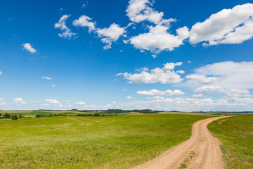 Single lane track running through green grassland with bold blue sky above.