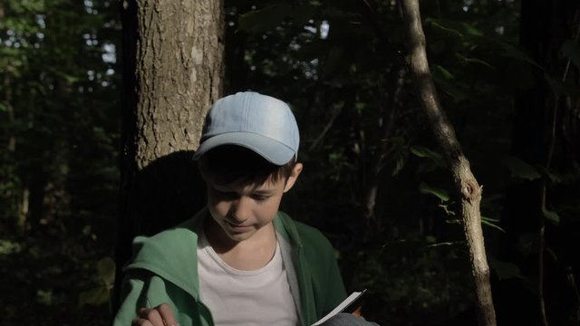 boy sits under a tree and reads a book with charts outdoors