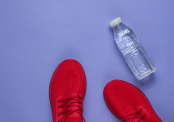 Training concept. Sport shoes, bottle water on purple background. Flat lay style. Copy space