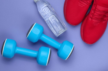 Training concept. Sport shoes, bottle water, dumbbells on purple background. Flat lay style.
