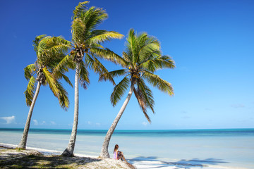 Woman sitting by the palm trees on the coast of Ouvea lagoon on Ouvea Island, Loyalty Islands, New Caledonia