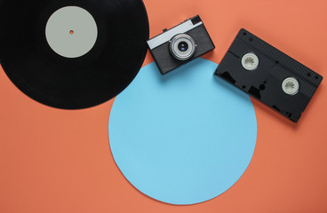 Retro vinyl record, video cassette, film camera on a coral color background with a blue circle. Top...
